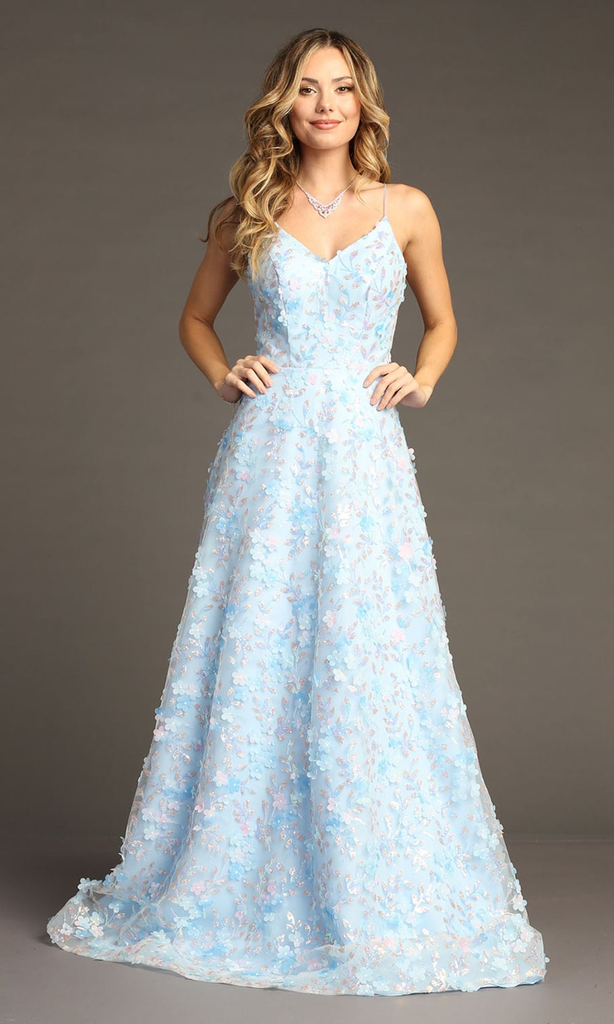 A woman models the Long Light Blue Floral Prom Dress: Chicas CHF3092, featuring 3-D flower details, standing against a plain gray background.